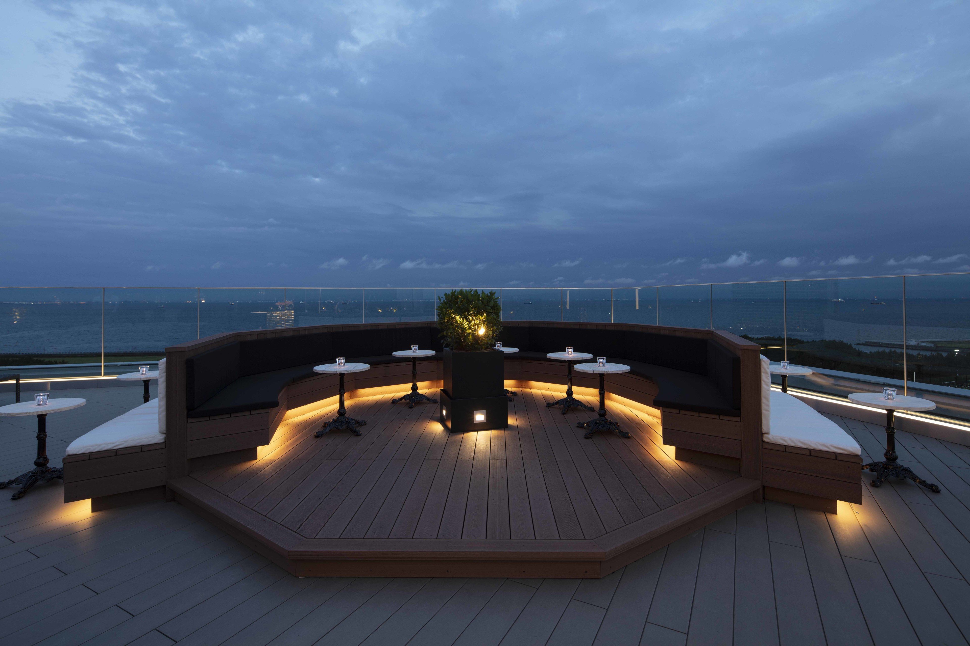A rooftop terrace with a wooden deck, seating areas, and tables.