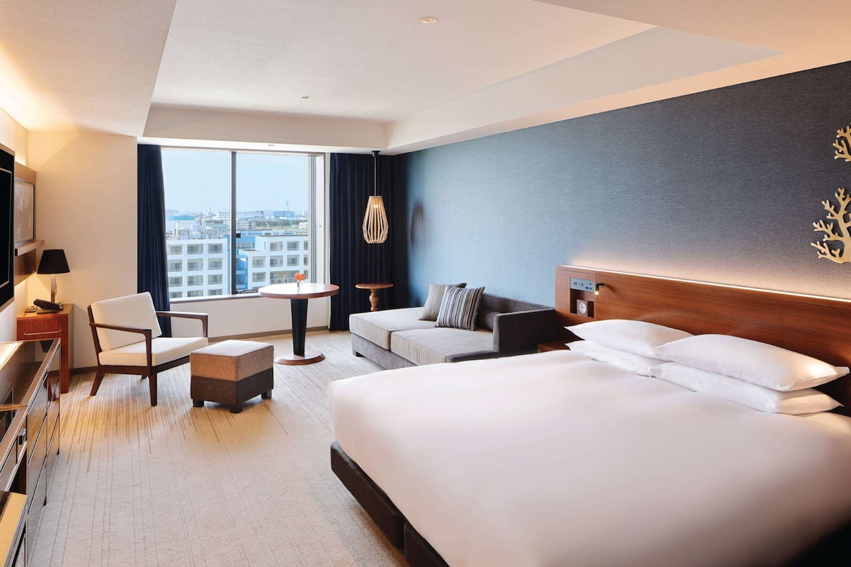 Ein Hotelzimmer mit einem großen Bett, einer Couch, einem Sessel, einem kleinen Tisch und einem Fernseher.