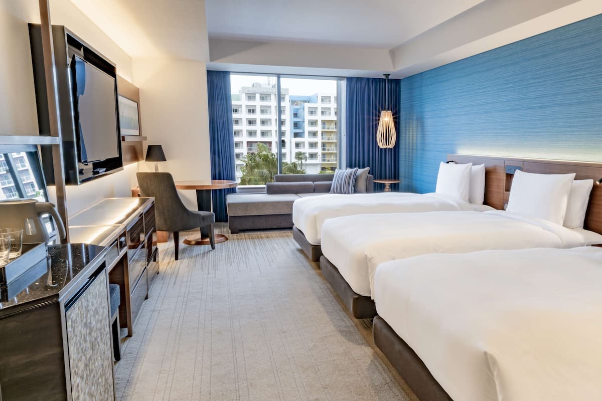 Ein Hotelzimmer mit einem großen Bett, einem Schreibtisch mit Fernseher, einer Sitzecke und Blick auf ein Gebäude.
