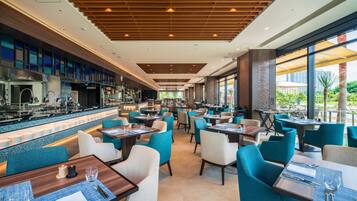 A modern restaurant with a bar area, multiple seating options, and large windows offering views of the outdoors.
