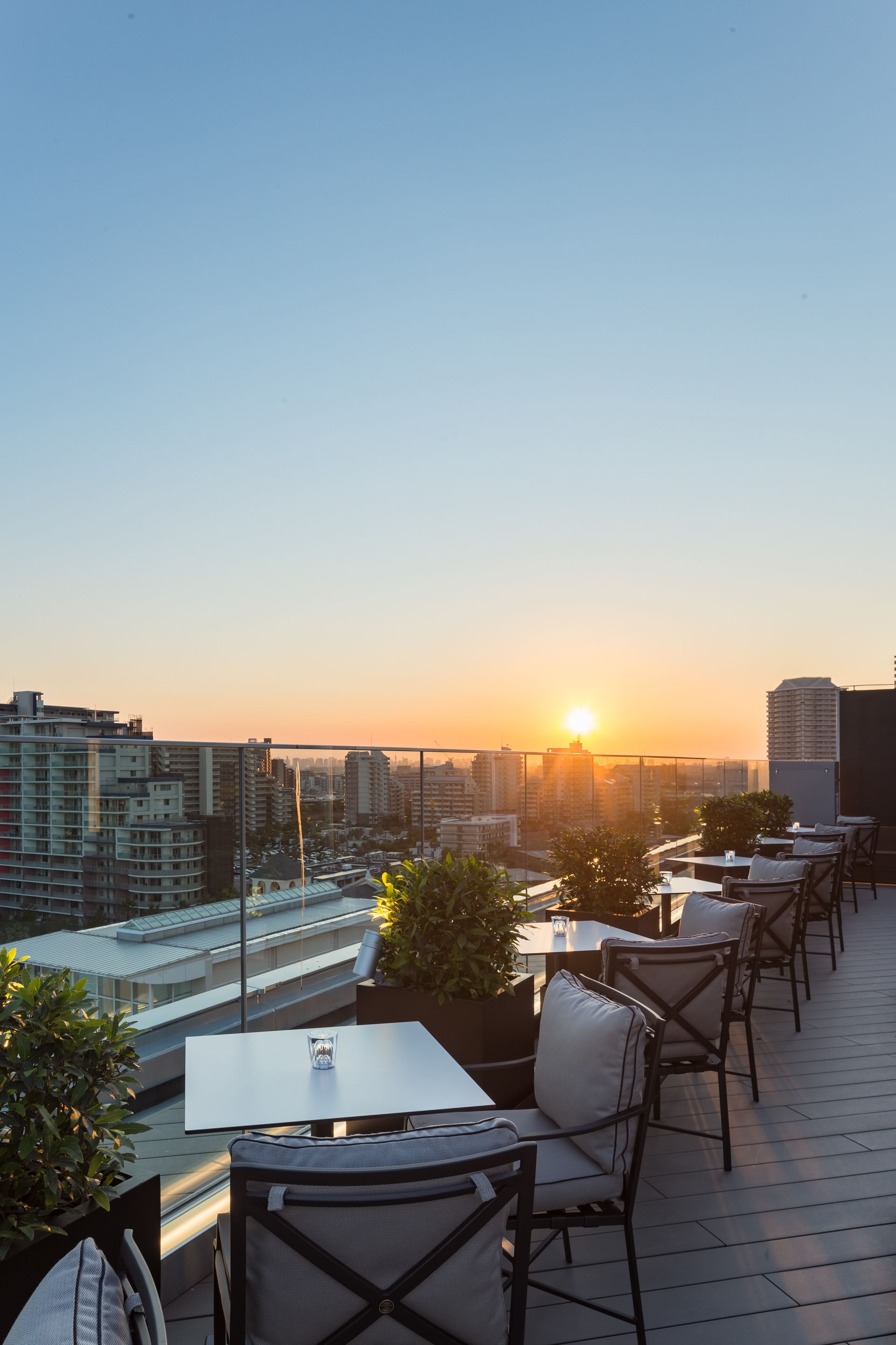 Terraza en la azotea con mesas y sillas, con vistas a un paisaje urbano al atardecer.