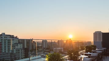 Terraza en la azotea con mesas y sillas, con vistas a un paisaje urbano al atardecer.