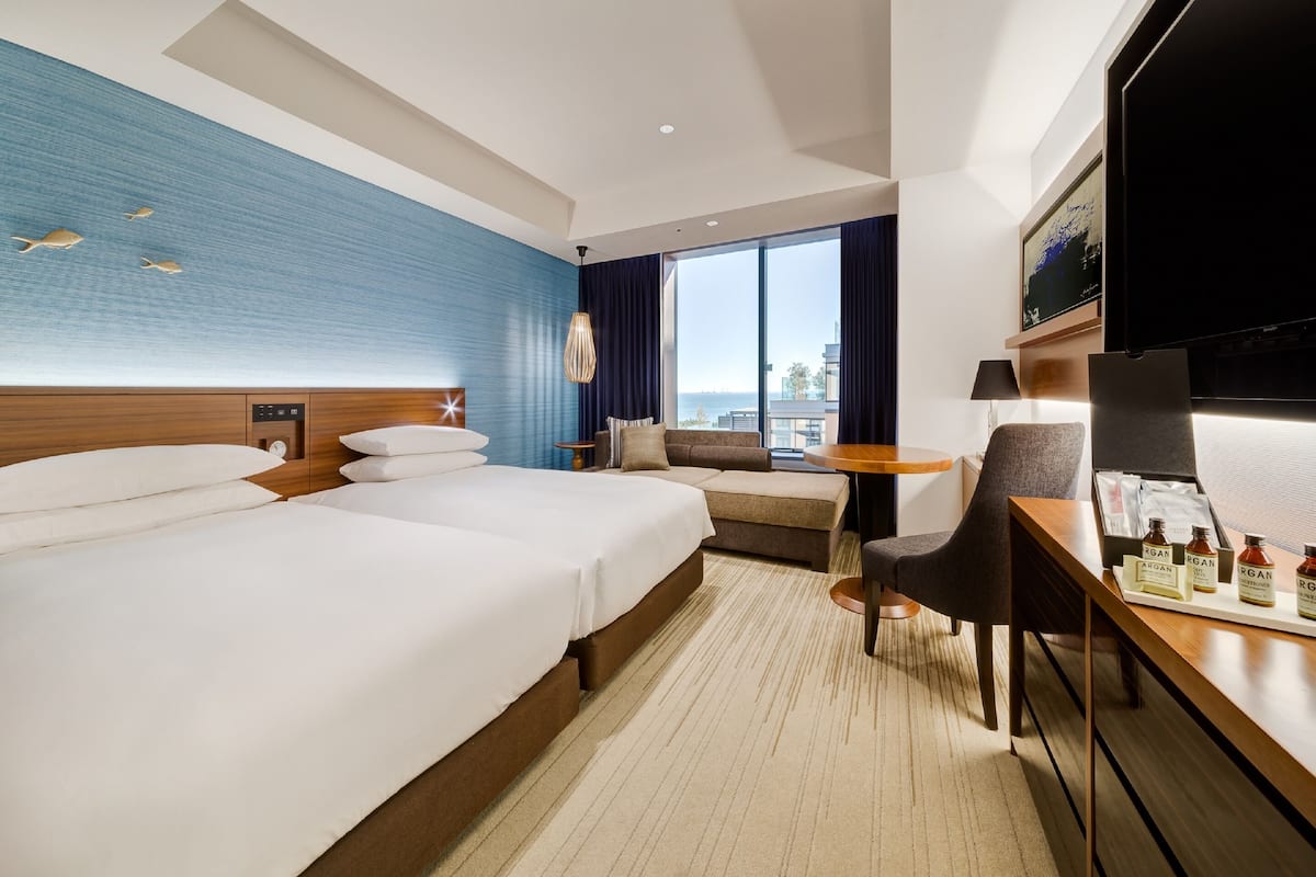 Ein Hotelzimmer mit zwei Betten, einem Schlafsofa, einem kleinen Tisch und einem Fernseher.