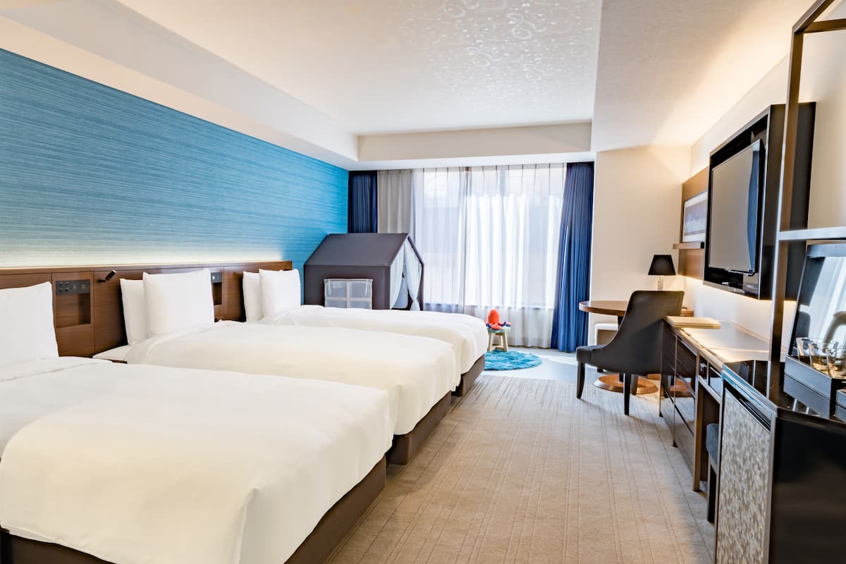 Ein Hotelzimmer mit zwei Betten, einem Schreibtisch, einem Fernseher und einer kleinen Sitzecke.