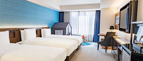 A hotel room with two beds, a desk, a television, and a small seating area.