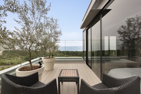 Un balcón con mobiliario de mimbre, un árbol en maceta y vista al mar.