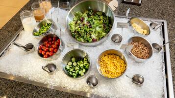 Un bufé con diversos alimentos como ensalada, tomates, pepinos, maíz y nueces sobre hielo.