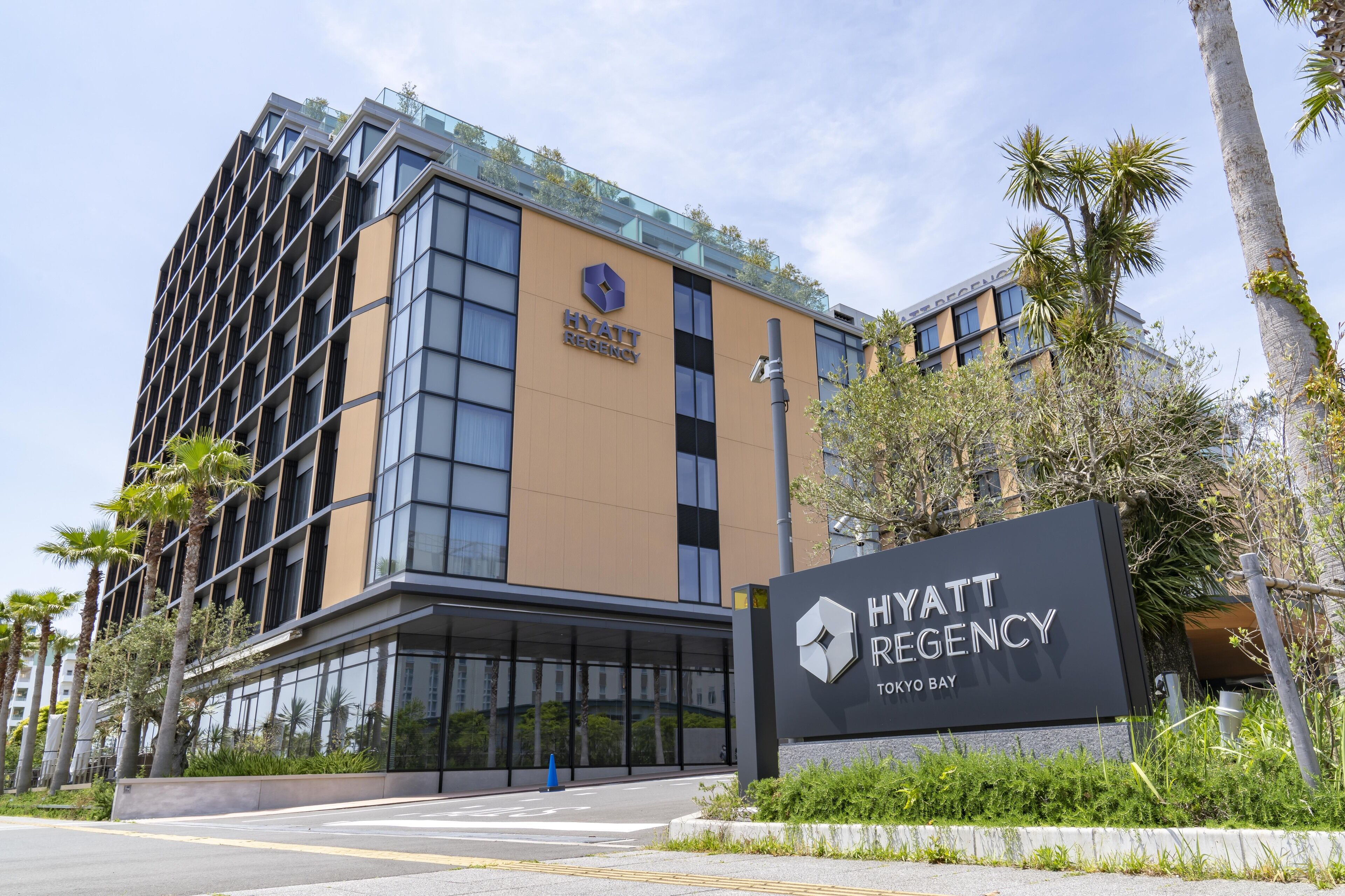 A modern Hyatt Regency Tokyo Bay hotel with a glass facade, a rooftop garden, and palm trees.