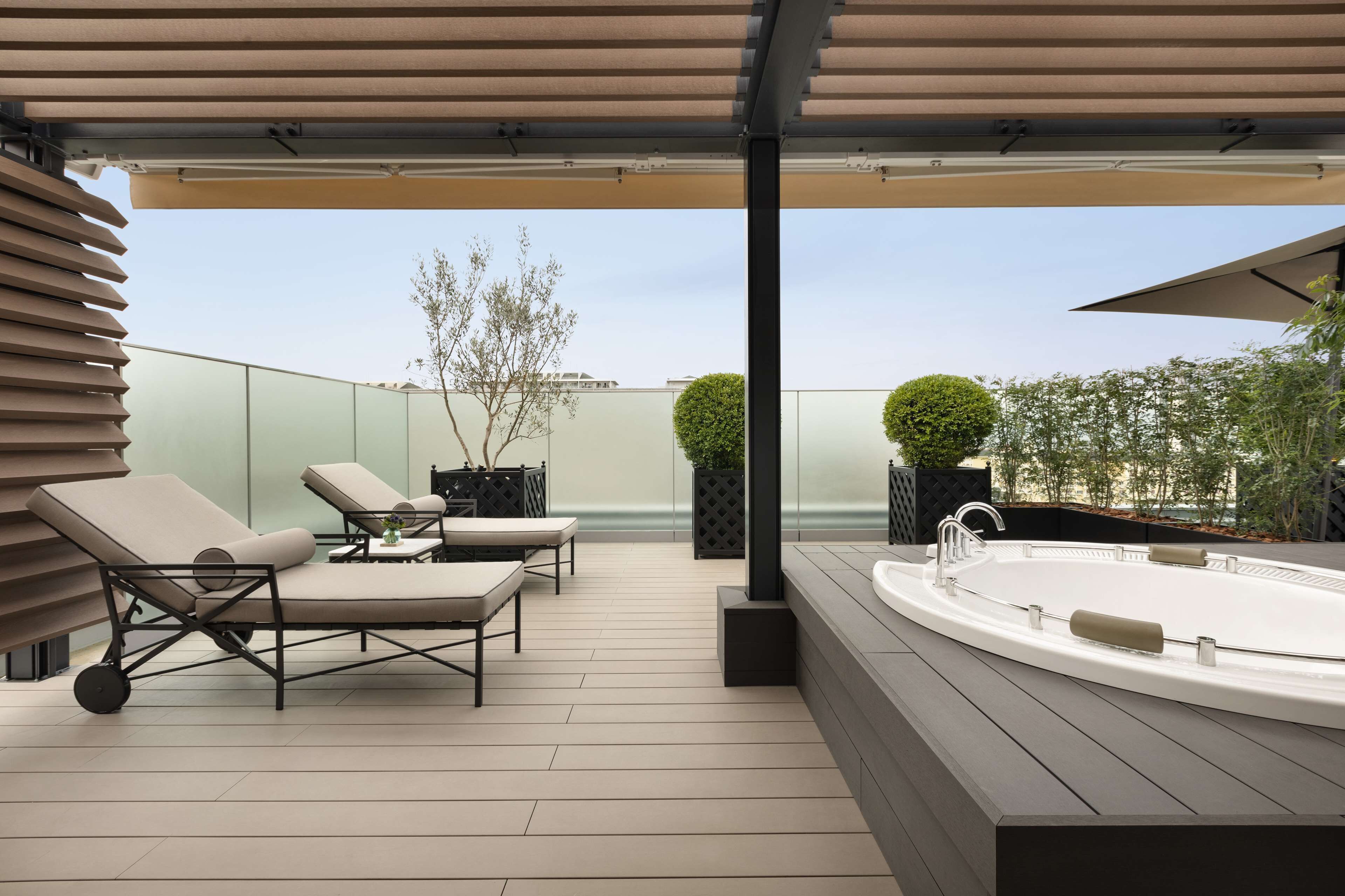 A modern outdoor patio with lounge chairs, a hot tub, and a pergola.
