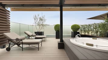 A modern outdoor patio with lounge chairs, a hot tub, and a pergola.