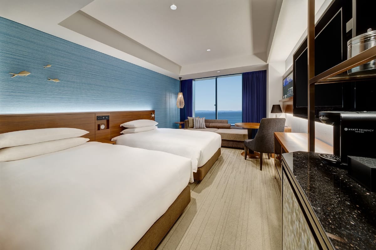 Ein Hotelzimmer mit zwei Betten, einem Schreibtisch, einem Stuhl, einem Fernseher und einem großen Fenster mit Blick.