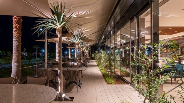 An outdoor patio area with tables and chairs, palm trees, and a glass wall. - Hyatt Regency Tokyo Bay (Urayasu)