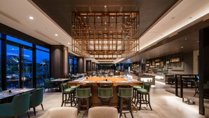 A modern dining area with a central bar, multiple seating options, and large windows offering views of the outdoors. - Hyatt Regency Tokyo Bay (Urayasu)