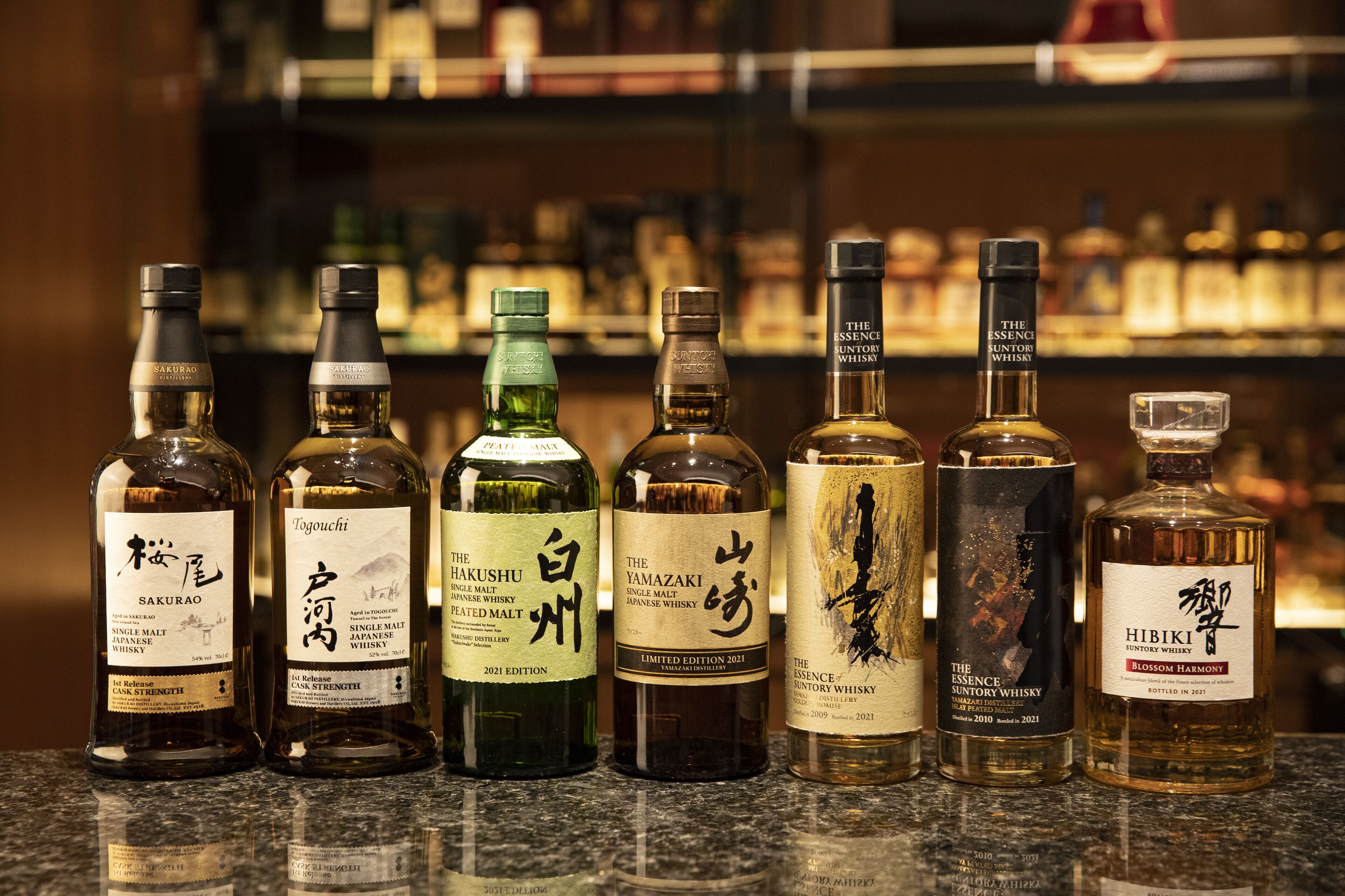 A selection of whiskey bottles on a counter with a blurred background of shelves.