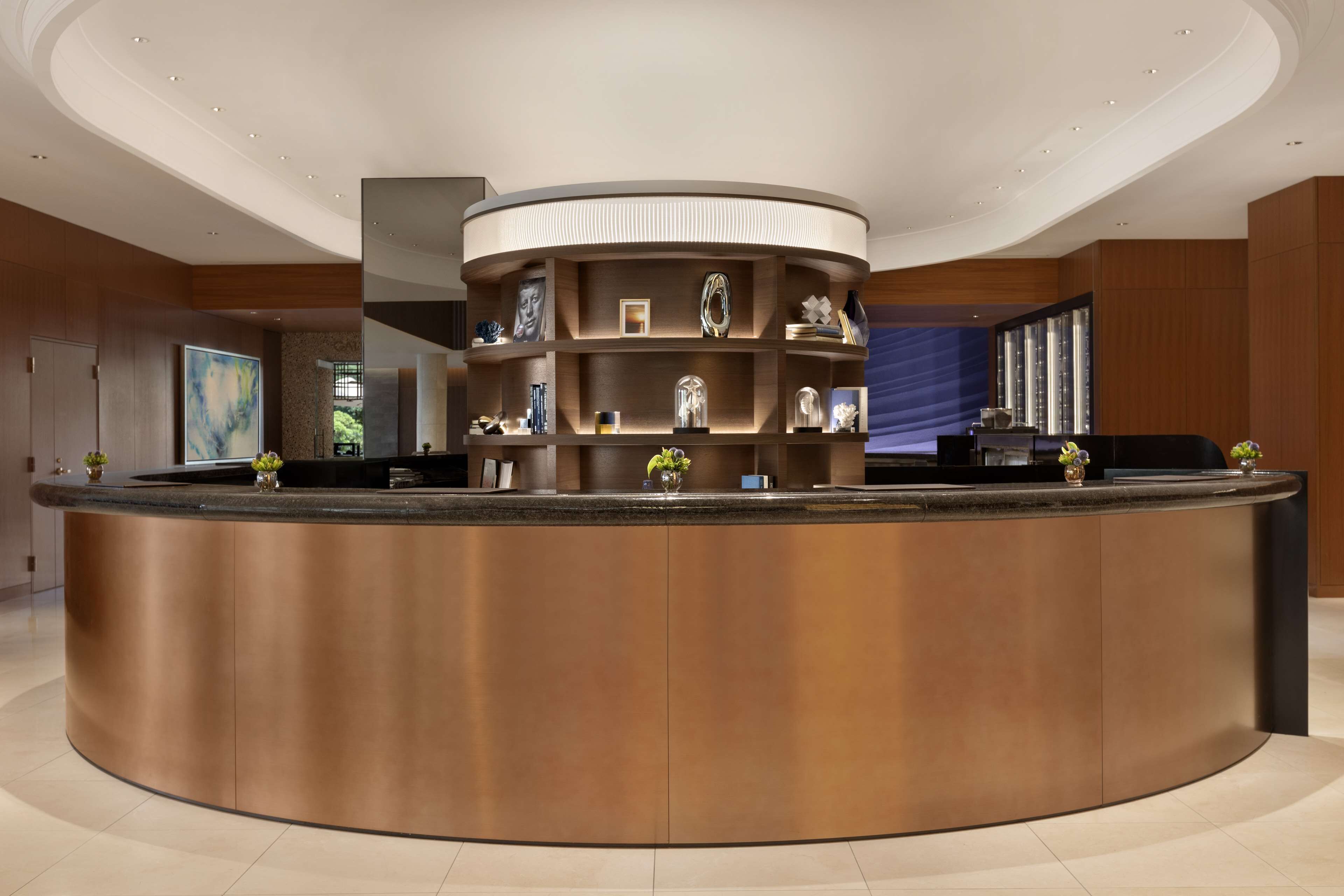 A modern reception area with a curved counter, built-in shelving with decorative items, and a large window in the background.