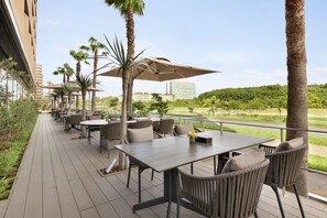 An outdoor patio with tables and chairs, palm trees, and a view of a hotel building in the background.