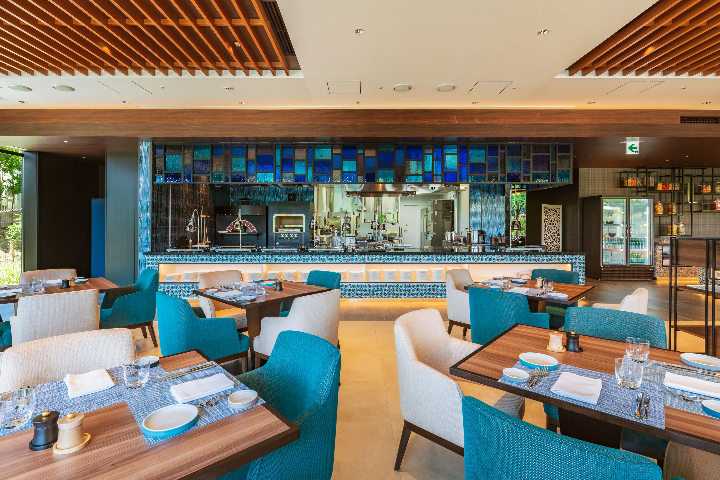 A modern restaurant with a bar area, blue-tinted glass partitions, and neatly arranged tables and chairs.
