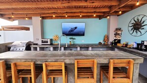 An outdoor kitchen with a TV, bar stools, and a grill.