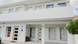 A two-story building with white exterior walls, multiple windows with red frames, and a small balcony.