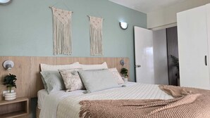 A bedroom with a bed, bedside tables, a wall-mounted macrame piece, and a door.