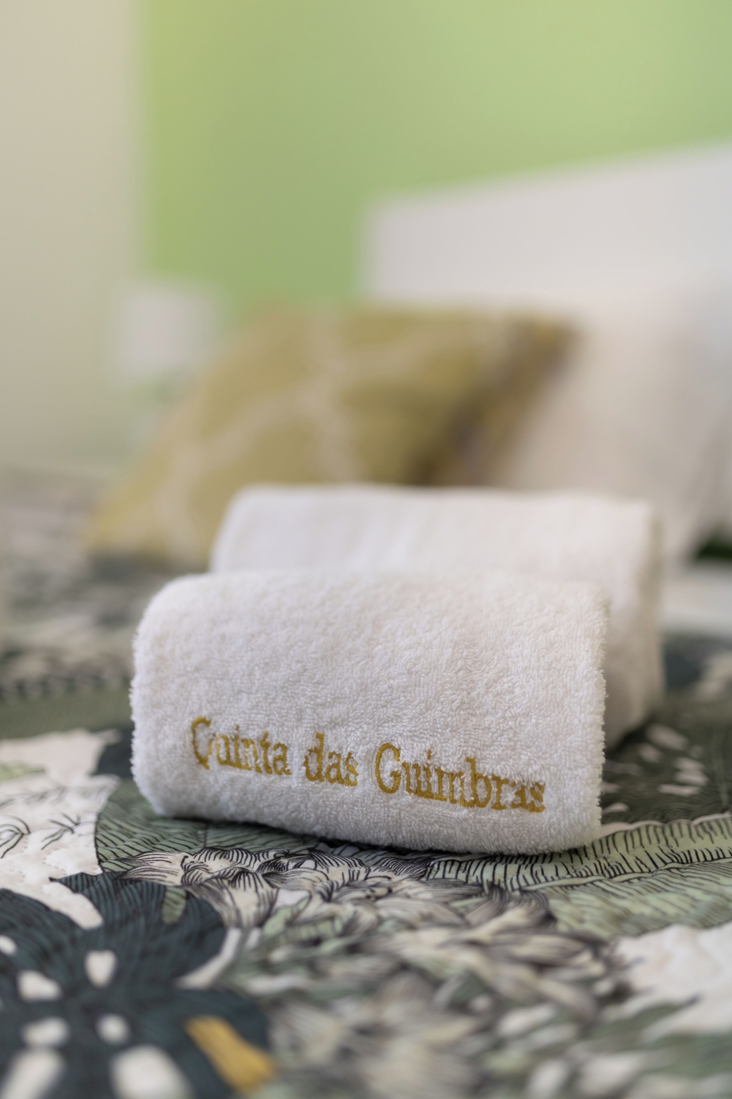 A neatly folded white towel with embroidered text on a patterned bedspread.