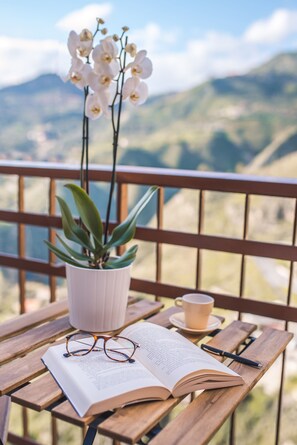 Un banco de madera con una orquídea en maceta, una taza y un libro abierto.