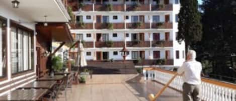 A hotel with a terrace, outdoor seating, and a person playing tennis.