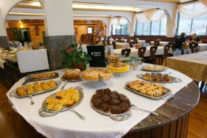 A buffet table with various dishes, a sign with the hotel name, and a view of the dining area. - Hotel 13 Linden (Treze Tilias)
