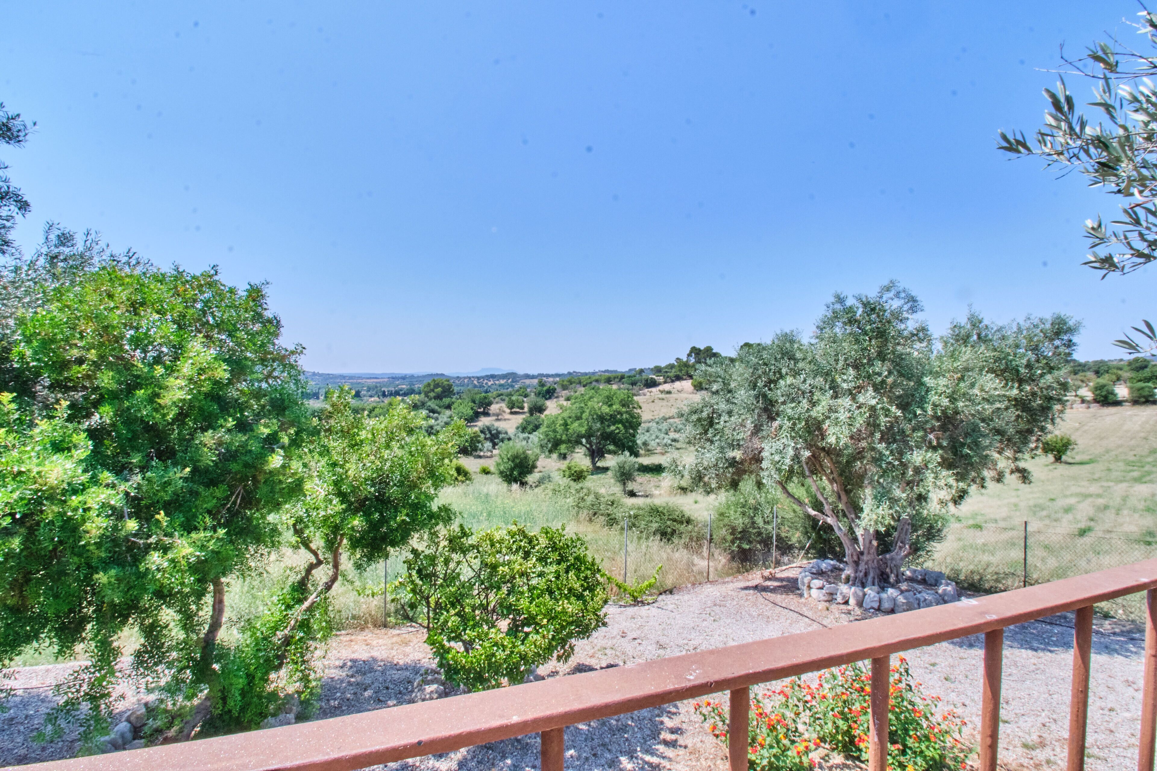 A view from a balcony with a railing, overlooking a rural landscape with trees and a clear sky.