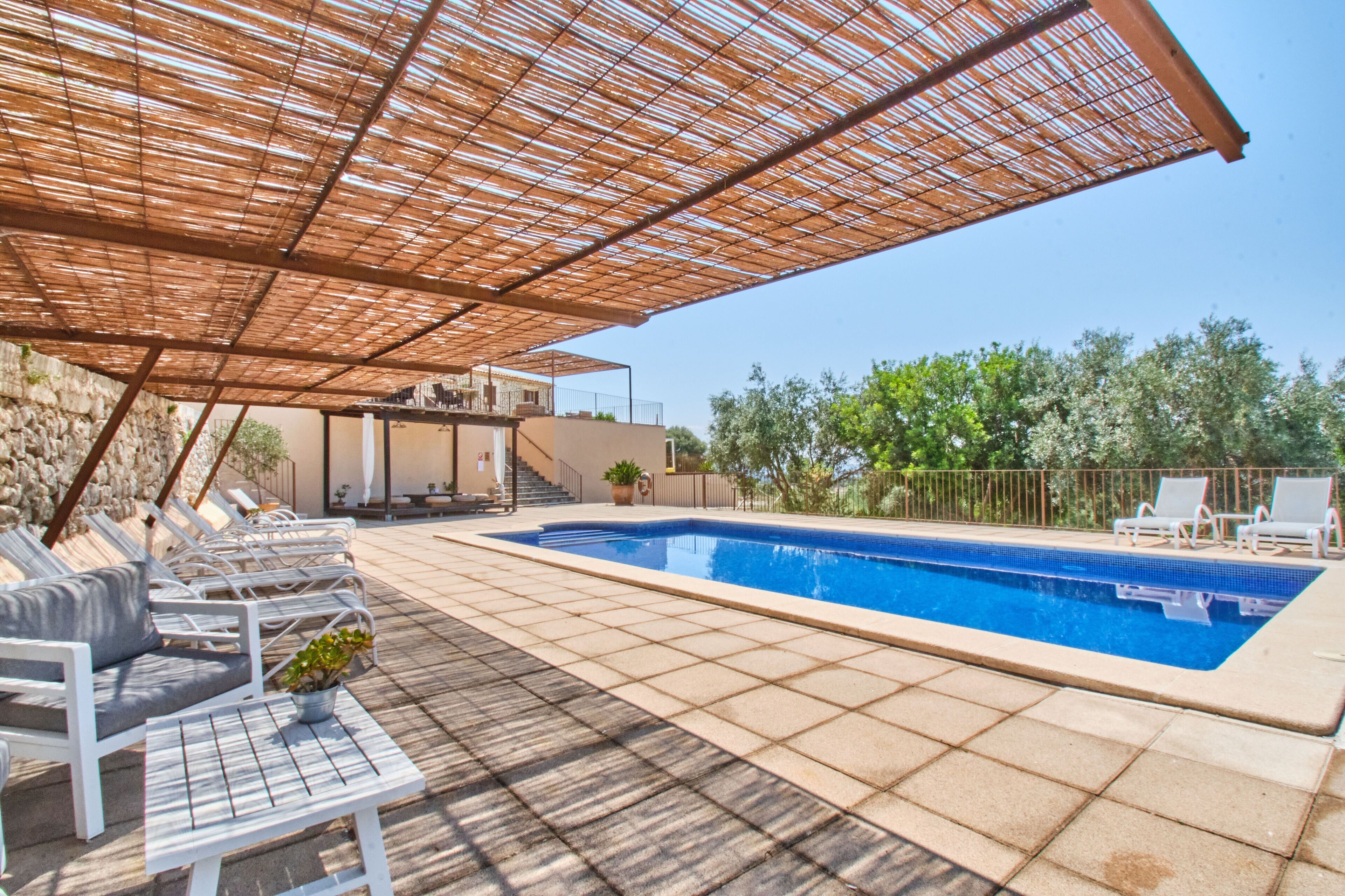 A swimming pool with a tiled deck, lounge chairs, and a pergola providing shade.