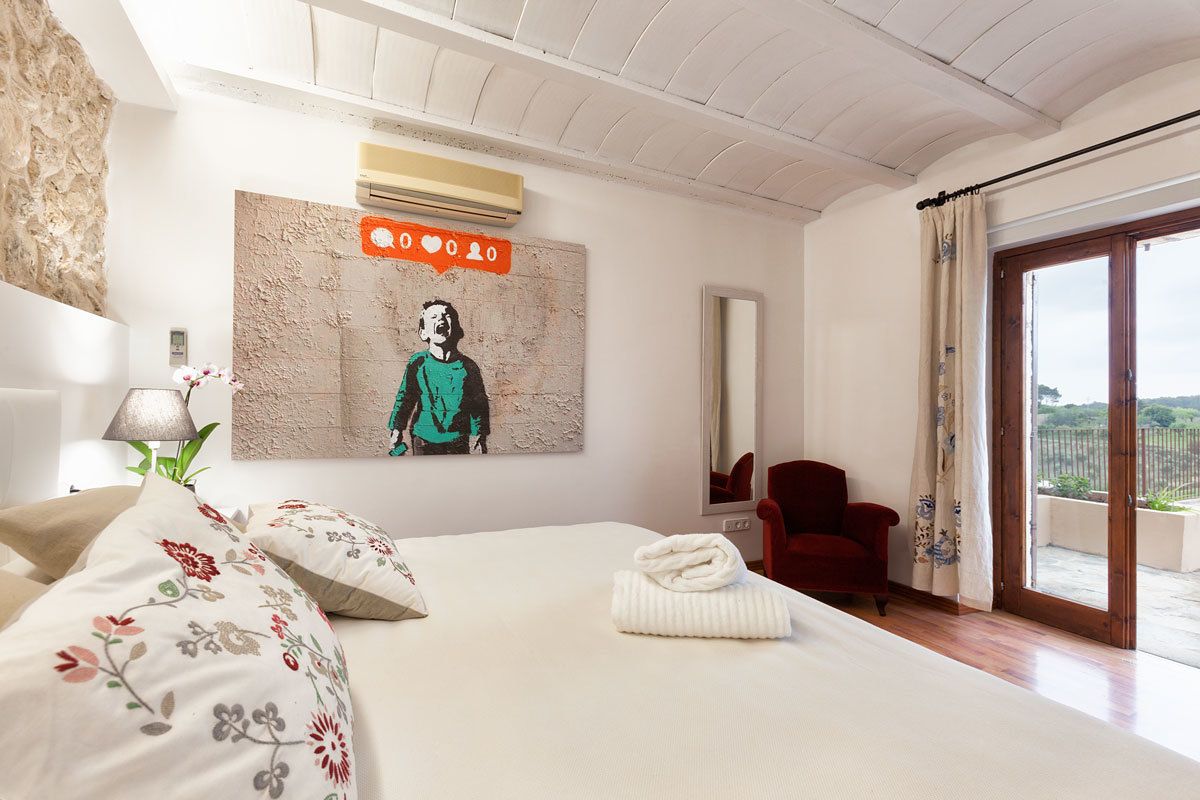 Un dormitorio con una cama, una silla roja, un cuadro y vistas a través de un ventanal.