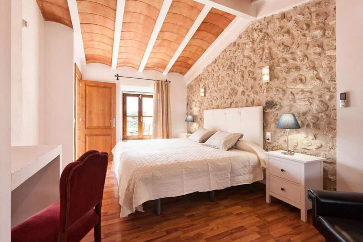 Un dormitorio con una cama grande, suelo de madera, pared de piedra y techo de madera.