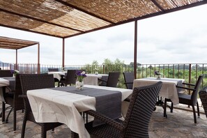 An outdoor patio with tables and wicker chairs, overlooking a scenic landscape.