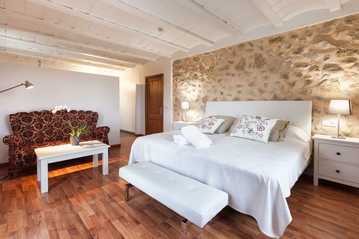 Un dormitorio con una cama grande, un banco, un sofá y una pared de piedra.