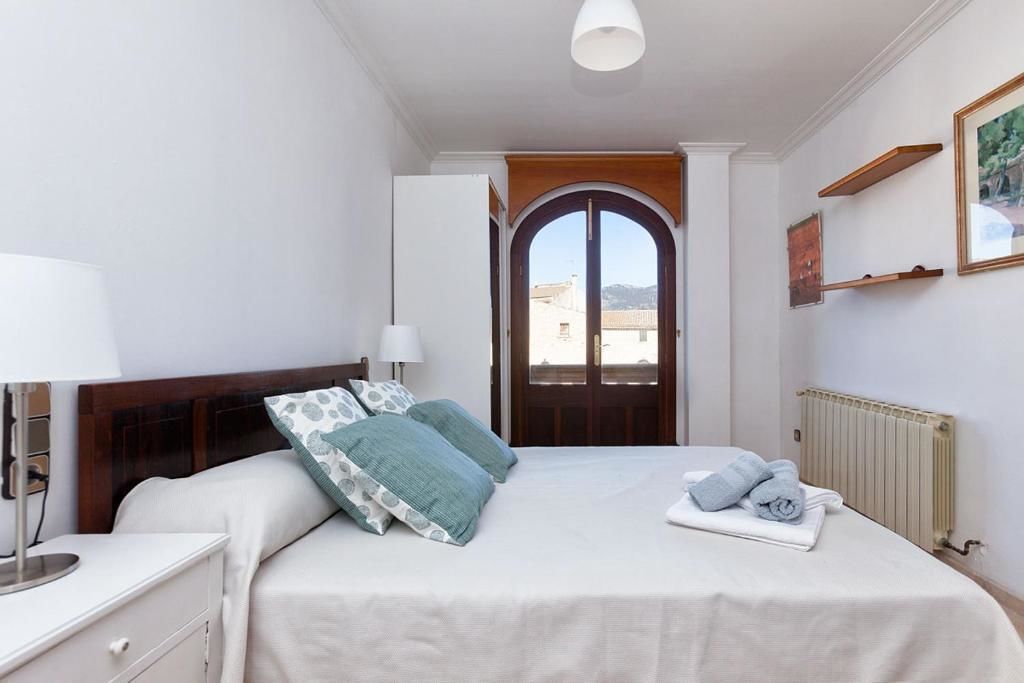 Een netjes ingerichte slaapkamer met een bed, nachtkastje, lamp en uitzicht buiten via een deur.