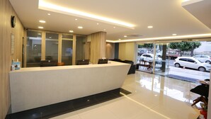Ein moderner Hotel-Empfangsbereich mit einer Rezeption, Sitzgelegenheiten und Blick auf parkende Autos.