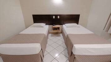 A hotel room with two single beds, a wooden nightstand, and a tiled floor.