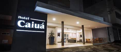 Entrada de hotel con diseño moderno, un gran letrero iluminado y una zona de recepción con asientos.