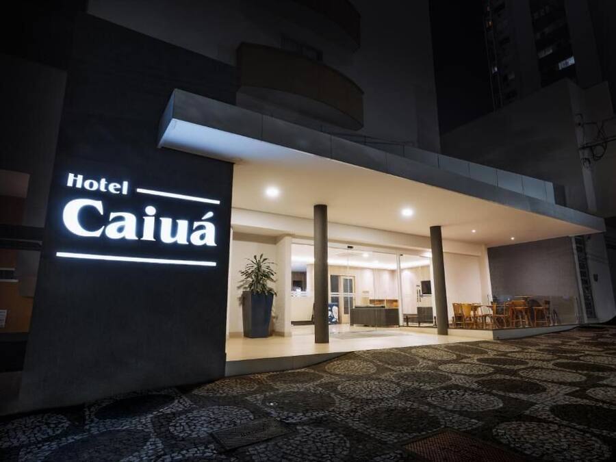 A hotel entrance with a modern design, a large illuminated sign, and a reception area with seating.