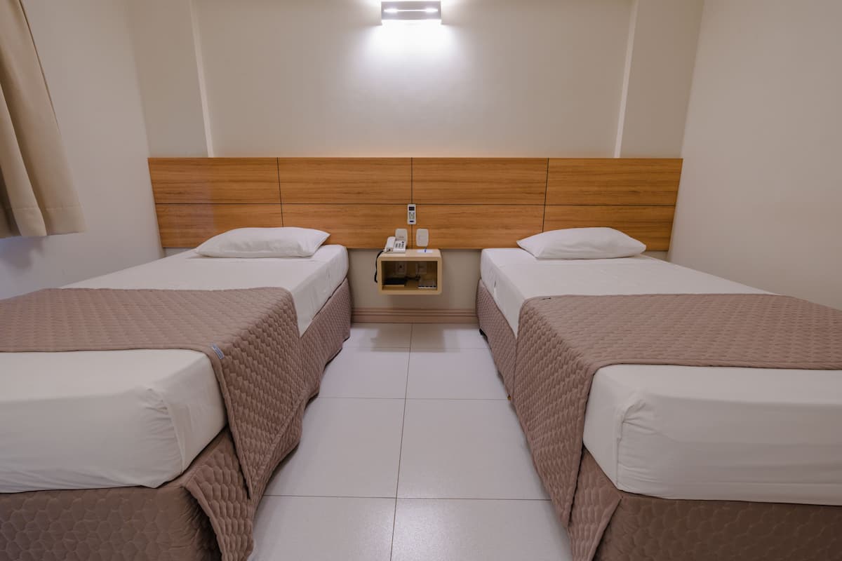 Habitación de hotel con dos camas, cabecera de madera, mesita de noche con teléfono y lámpara sobre la cama.