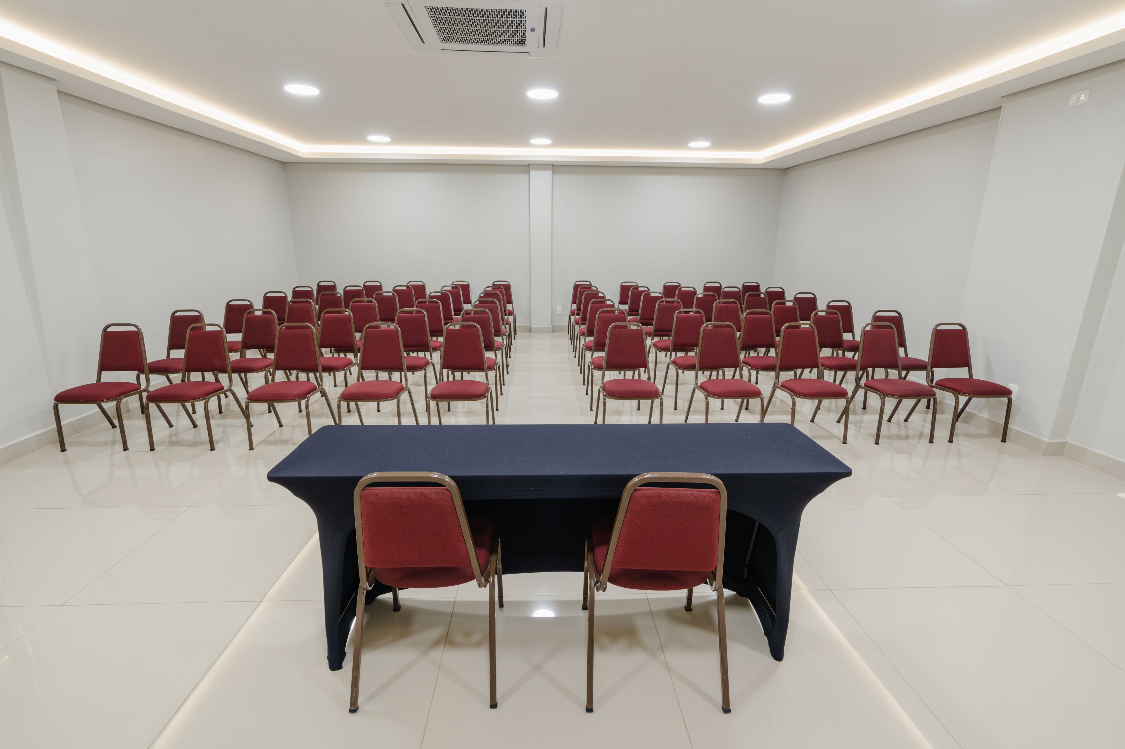 A conference room with a long table and rows of red chairs.