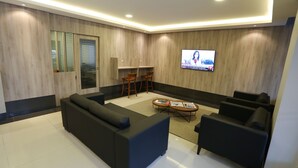 Ein modernes Wohnzimmer mit einer Couch, Sesseln, einem Couchtisch und einem an der Wand befestigten Fernseher.