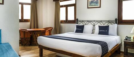 A hotel room with a wooden bed, a small table with chairs, and a painting on the wall.