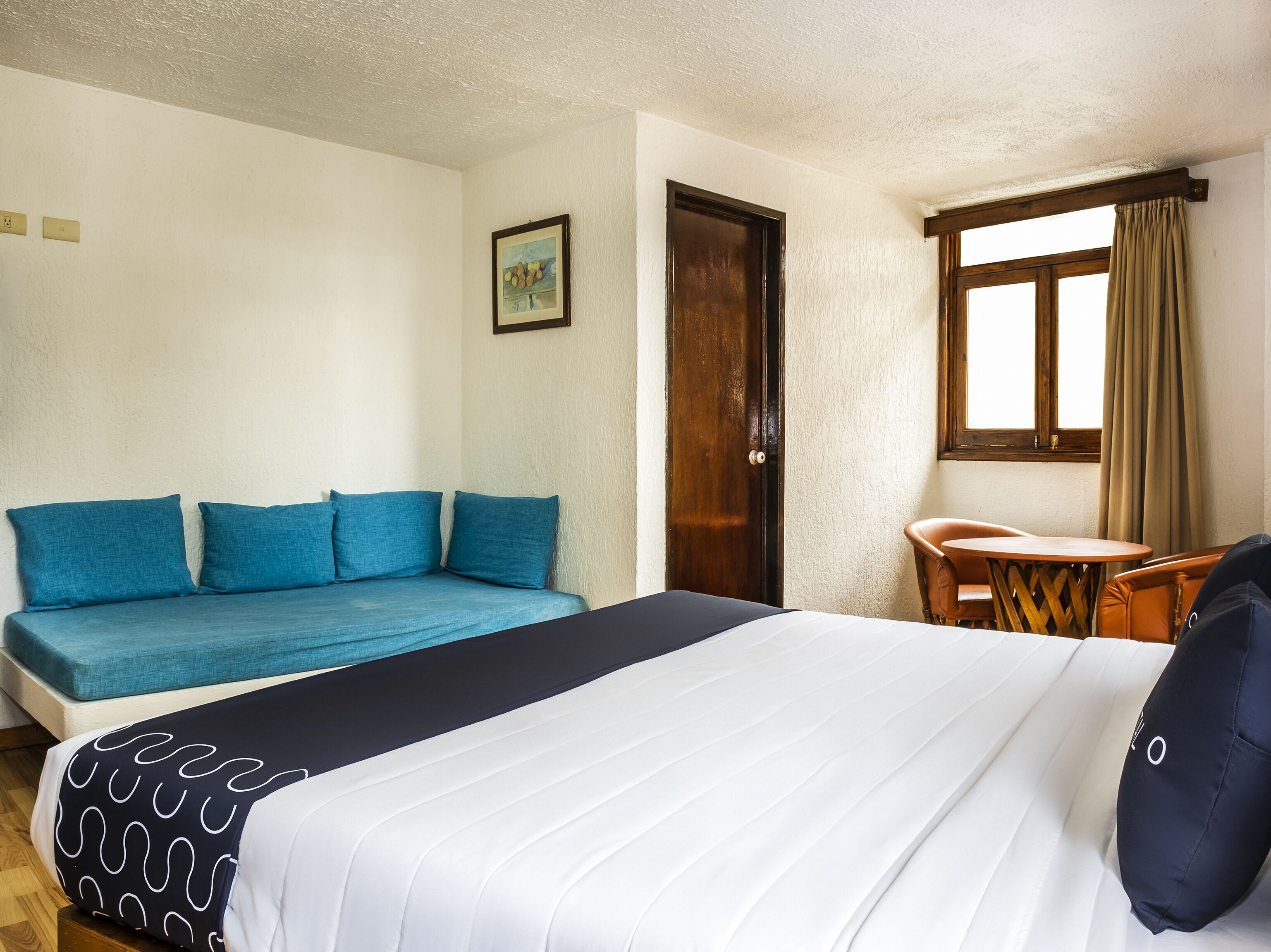 A hotel room with a bed, a sofa, a small table, and a window with curtains.