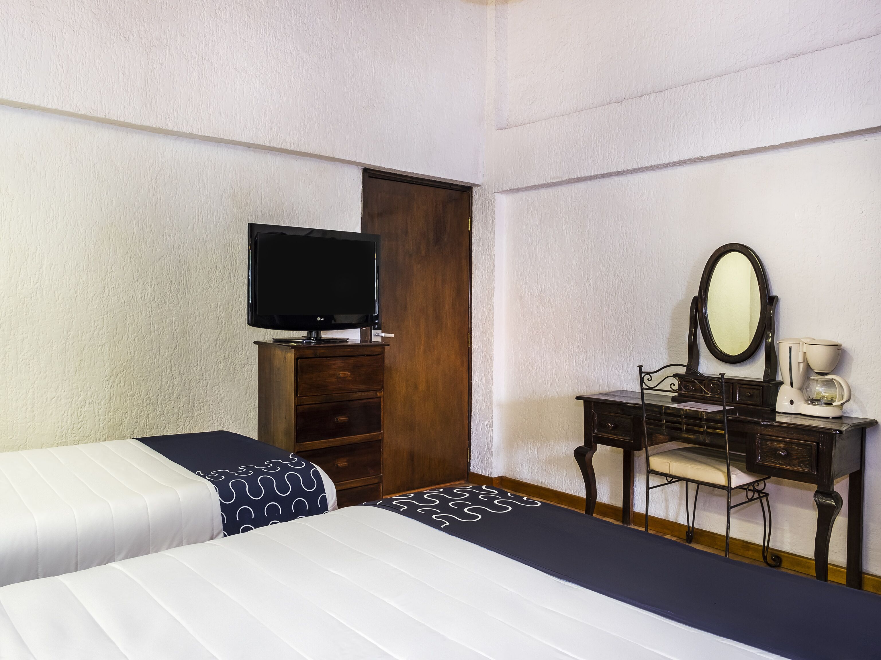 Habitación de hotel con dos camas, un aparador de madera, televisor, espejo y cafetera.