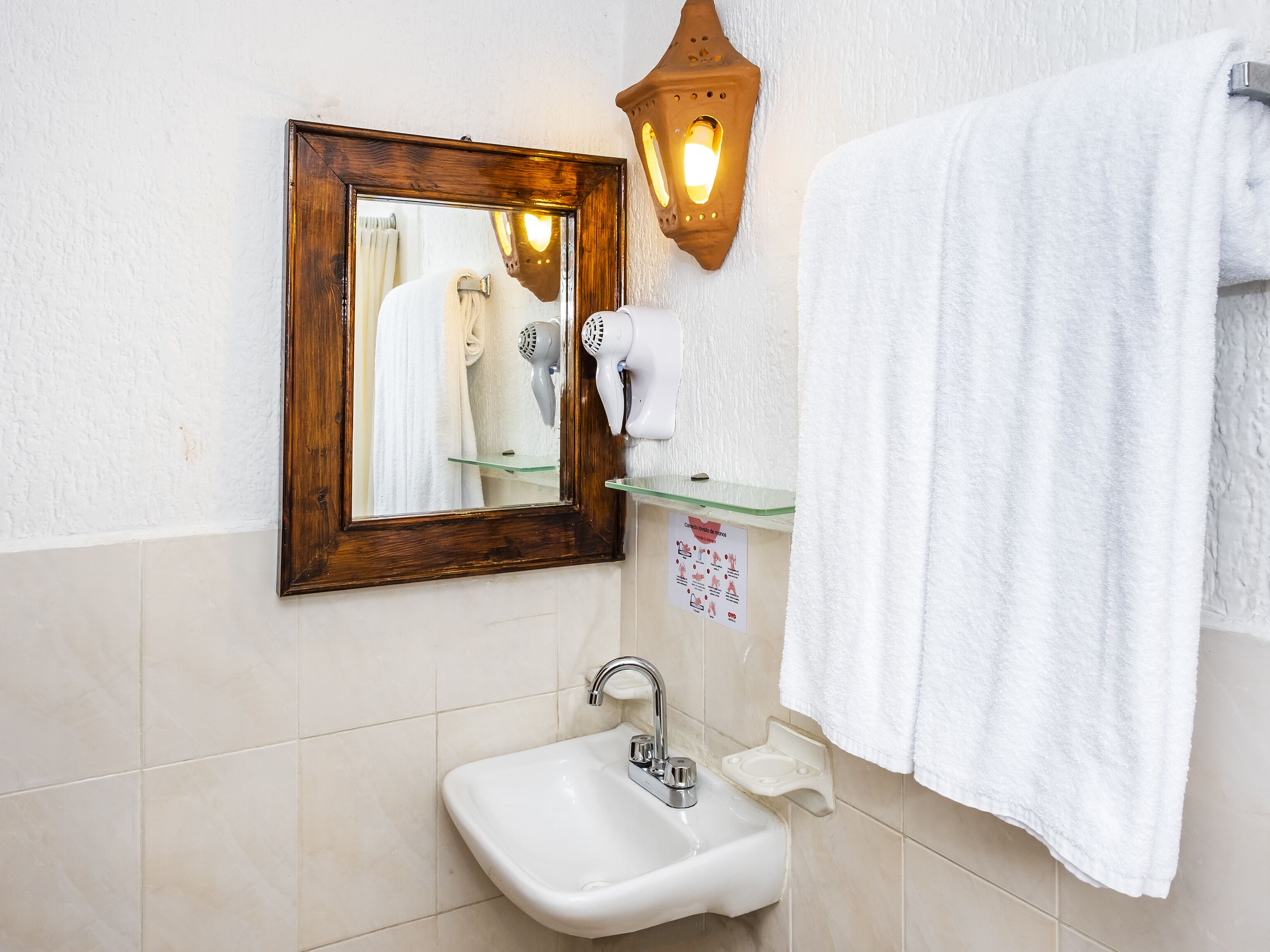 A bathroom with a sink, mirror, towel rack, and a wall-mounted hairdryer.