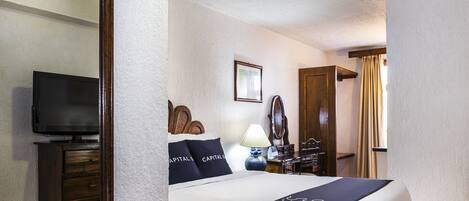 Habitación de hotel con una cama, televisión, cómoda, espejo y ventana con cortinas.