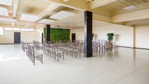 Tilava aula, jossa on riveissä järjestettyjä tuoleja tapahtumaa varten, suuri pylväs ja vihreä seinä, jossa on kasveja.