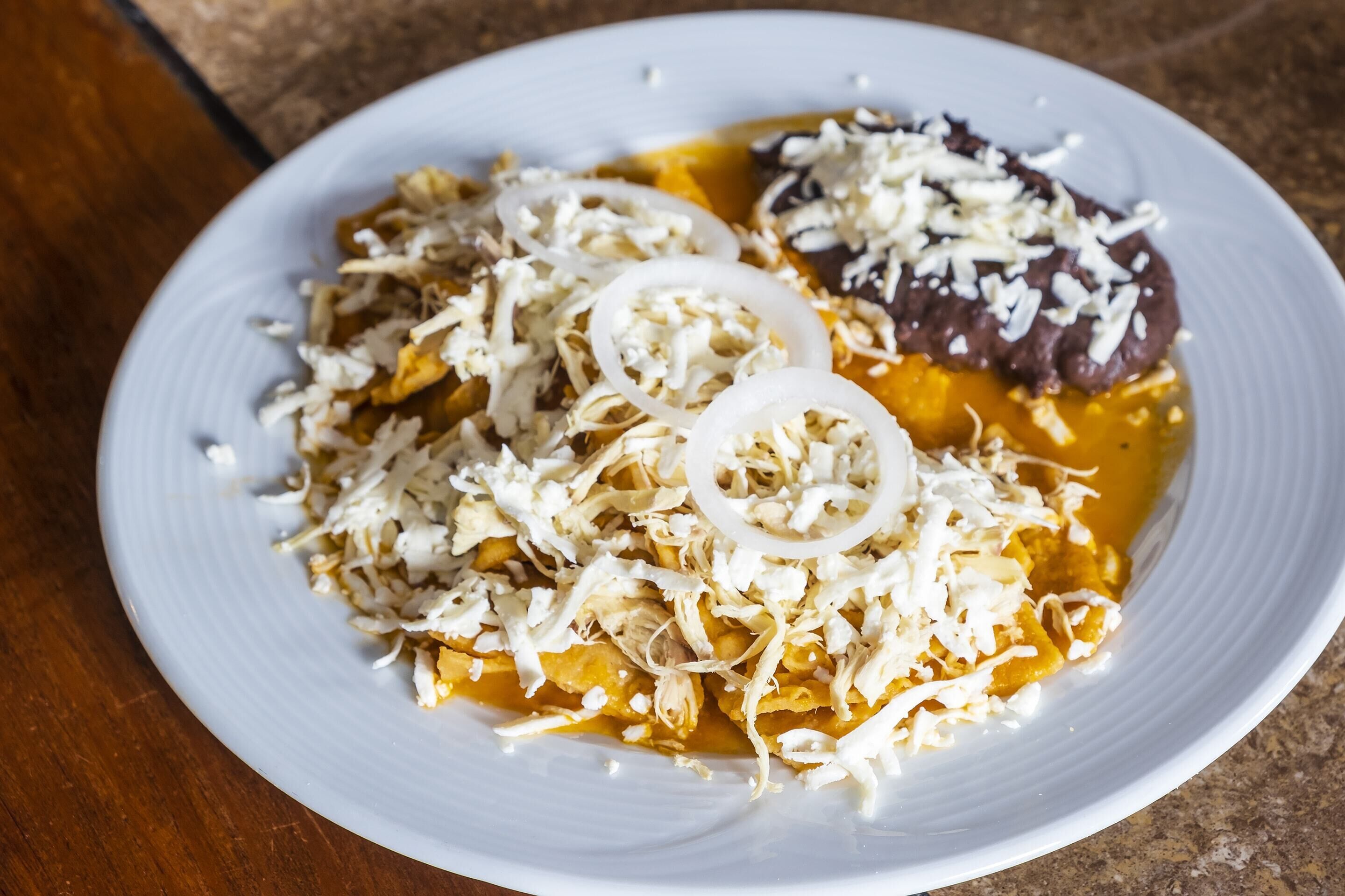 A plate of nachos topped with shredded cheese, sliced onions, and a dark sauce.