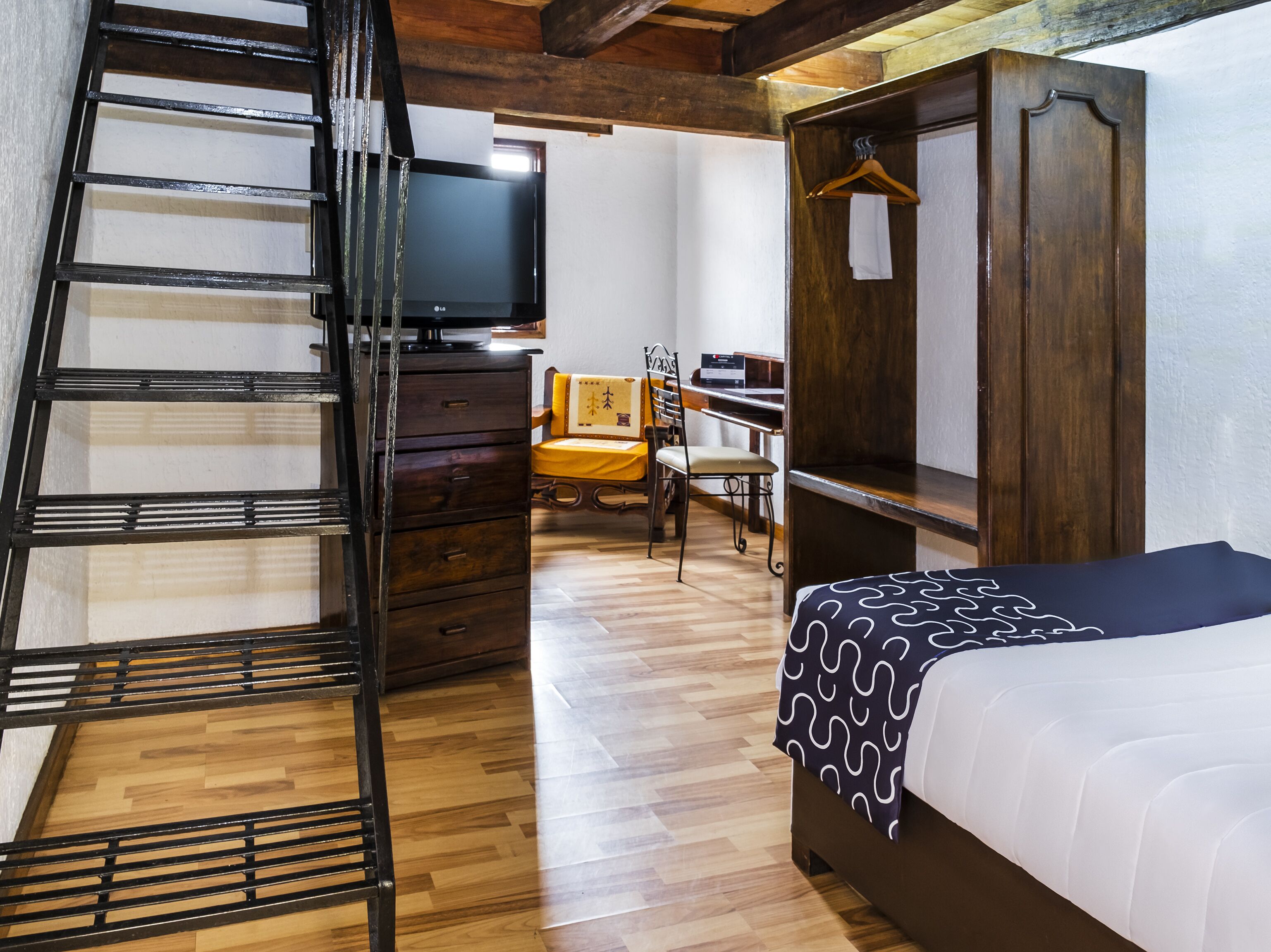 A bedroom with a bed, a dresser, a chair, a desk, a television, and a wooden staircase.